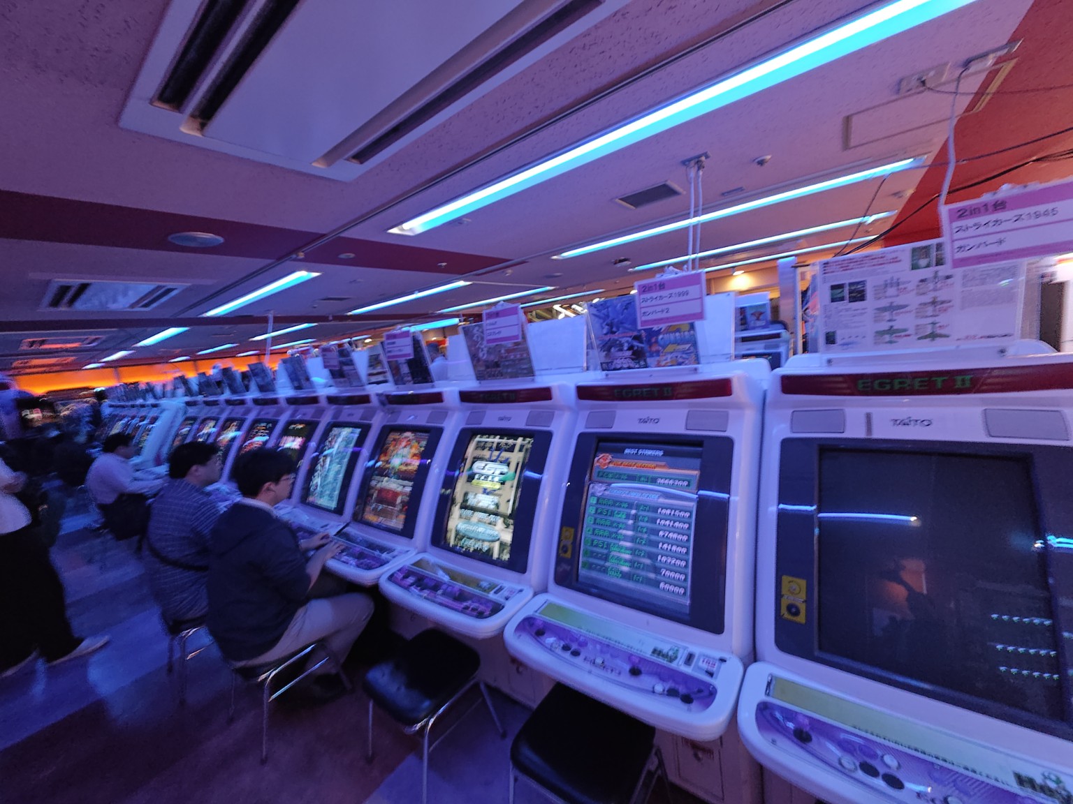 Rows of white arcade cabinets at Hey, with players seated in front of the screens.